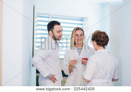 Mature Doctor Discussing With Nurses In A Hallway Hospital. Doctor Discussing Patient Case Status Wi