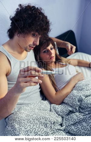 Portrait Of Young Man Showing Temperature In Thermometer To Sick Woman Lying On Bed. Sickness And He
