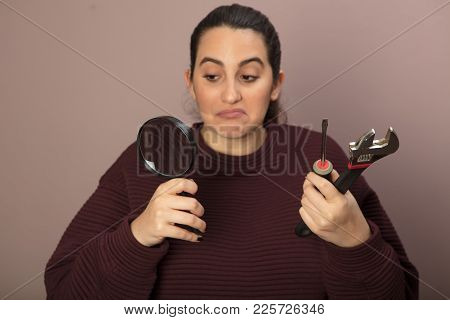 Thoughtful Woman As She Holds A Spanner, A Hammer And Manifying Glass In Her Hands In A Diy Concept