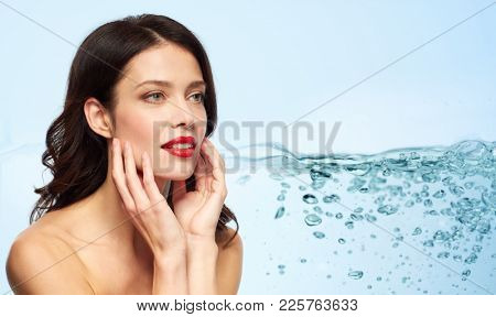 beauty, make up and people concept - happy smiling young woman with red lipstick touching her face over blue background with bubbles in water splash