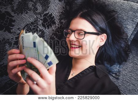 Happy Girl Lying On A Bed With Euro Money In Her Hands. Female Or Young Woman.