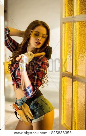Attractive Workwoman With Tool Belt And Hammer Posing On Construction