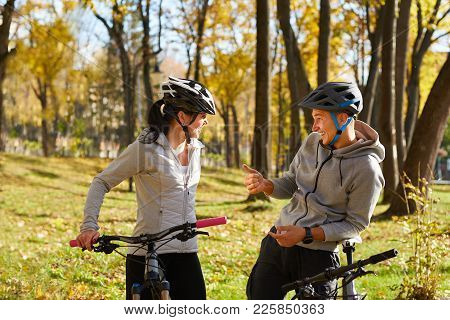 Happy Young Couple Having Fun Riding A Bicycle On Sunny Autumn Day In The Park. Two People Are Talki