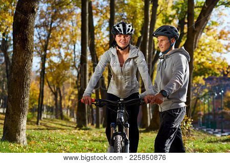 Happy Young Couple Having Fun Riding A Bicycle On Sunny Autumn Day In The Park. Two People Are Talki