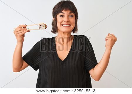 Young beautiful woman eating sushi using chopsticks standing over isolated white background screaming proud and celebrating victory and success very excited, cheering emotion