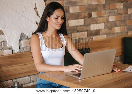 Attractive Smart Girl Working On Laptop In Cafe. Beautiful Girl Using Computer For Work. Girl Grinki
