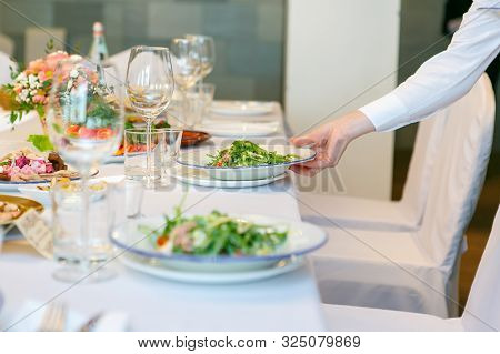 A Close Up Of The Waitress Hand Serves The Green Salad Dish On The Banquet Table In The Rastaurant