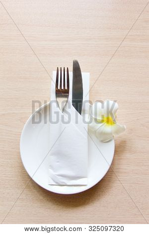 Knife And Fork Wrapped In A Napkin Lying On A White Plate Decorated With A Flower Plumeria. The View