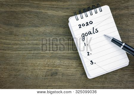 Top View 2020 Goals List On Notepad. Handwriting On Memo Paper Notebook With Black Pen Over Wooden T