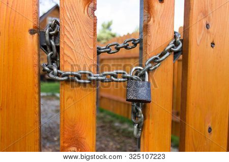 Padlock And Steel Thick Chain On A Bright Yellow Wooden Fence