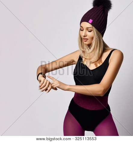 Portrait Of Stylish Blonde Woman In Purple Sports Wear Bodysuit And Leggings And Winter Hat Standing