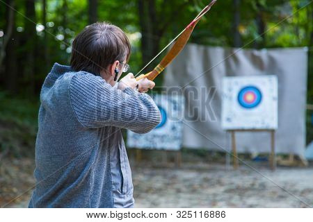 Male Archer Shooting Targets With Wooden Bow At Historical Festival. Archery And Medieval Culture Co