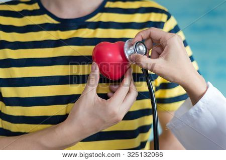 Woman Doctor Using Stethoscope Listen Heart Beat Sound From Red Heart Plastic On Hand Of Patient. Co