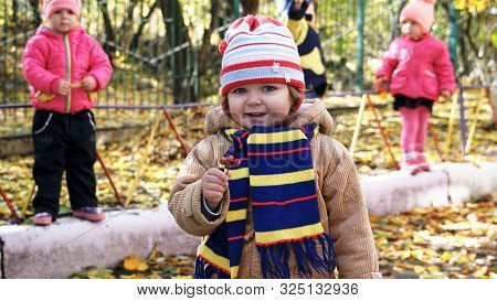 Autumn Time. Little Smiling Child With Bunch Of Ashberry Dressed In Yeallow Jacket And Striped Scarf