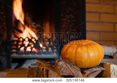 Halloween Pumpkin Lies On Birch Wood In Front Of A Blazing Fireplace. Mystical Holiday Halloween.