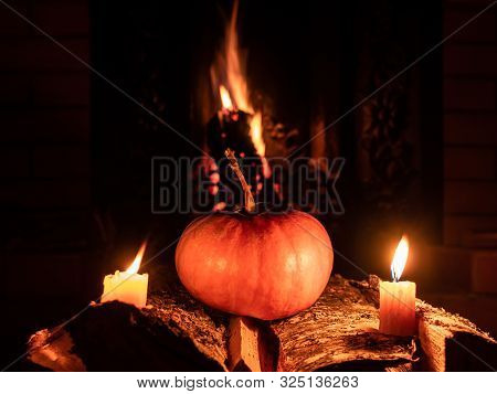Halloween Pumpkin In The Dark On Birch Logs Next To Burning Candles. In The Background Is A Flame Fr