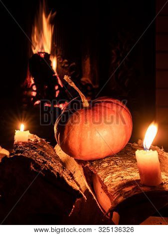 Halloween Pumpkin In The Dark On Birch Logs Next To Burning Candles. In The Background Is A Flame Fr
