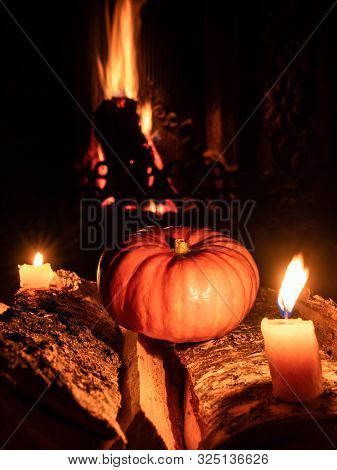 Halloween Pumpkin In The Dark On Birch Logs Next To Burning Candles. In The Background Is A Flame Fr