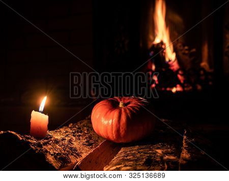 Halloween Pumpkin In The Dark On Birch Logs Next To Burning Candles. In The Background Is A Flame Fr