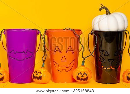 Three Halloween Themed Buckets With Jack O Lantern Lights And A White Pumpkin On An Orange Backgroun