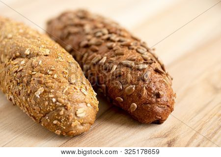 Long Whole Wheat Sunflower Seed Bread Roll And Long Whole Wheat Sesame Seed Bread Roll On Light Wood