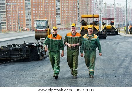 tres trabajadores de la construcción de la carretera feliz caminar sobre máquina pavimentadora de asfalto