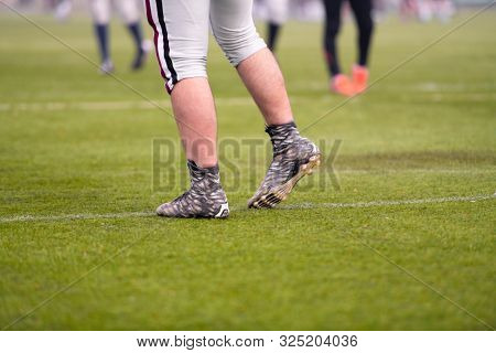 close up shot of group young professional american football players warming up and stretching together before a practice on the field  focus on the legs