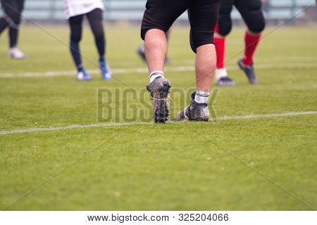 close up shot of group young professional american football players warming up and stretching together before a practice on the field  focus on the legs
