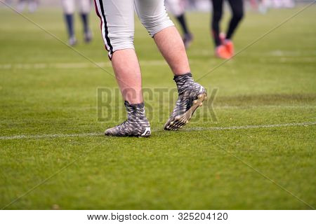 close up shot of group young professional american football players warming up and stretching together before a practice on the field  focus on the legs