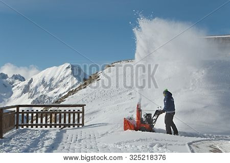 LES ORRES, FRANCE - JANUARY 22, 2015: Man plowing snow after fresh snowfall in the mountains at restaurant at Les Orres ski resort. The outdoor terrace has a magnificent view over the Alpine landscape
