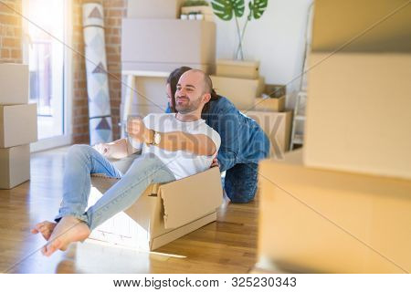 Funny and crazy couple having fun riding a cardboad box as a car, smiling happy and lauging at new home