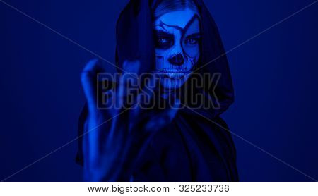 Creepy Witch In Hooded Cape Gesturing And Jinxing Camera While Standing Under Blue Light During Hall