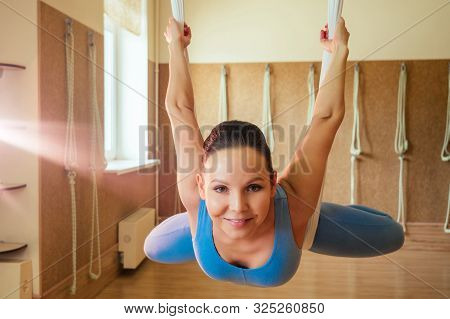 Portrait Of A Beautiful Young Woman Engaged In Anti-gravity Yoga On Canvases. Yoga On The Hammock. T