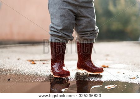 Little Girl In Red Rainboots Playing In Puddle After Rain. Happy Fall Childhood Activity