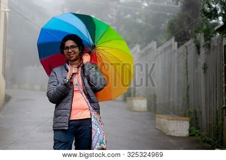 Young Indian Girl With A Colorful Umbrella Standing On A Foggy Street In Himachal Pradesh