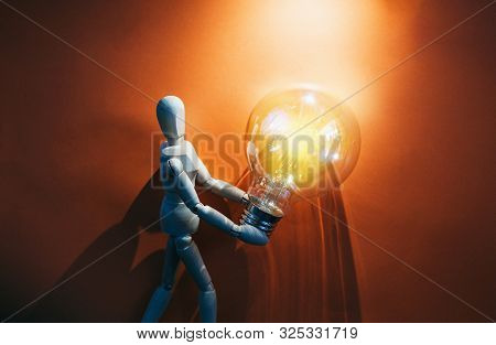 Wooden Puppet With Light Bulb In Orange Background.wooden Mannequin Figure Taking The First Step To 