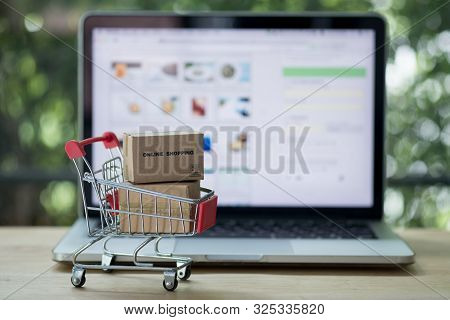Miniature Cardboard Boxes In Shopping Cart With Laptop Computer. Concept Of Online Shopping
