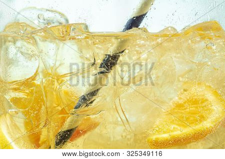 Close Up Of Lemon Slices In Stirring The Lemonade And Ice Cubes On Background. Texture Of Cooling Sw