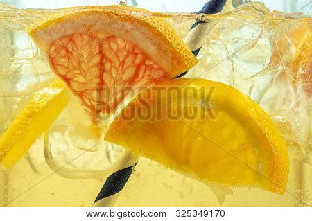 Close Up Of Lemon Slices In Stirring The Lemonade And Ice Cubes On Background. Texture Of Cooling Sw