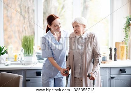 Smiling Caregiver Helping Aged Woman To Make Steps