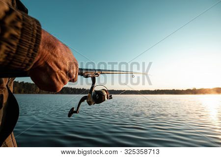 Hands Of A Man In A Urp Plan Hold A Fishing Rod, A Fisherman Catches Fish At Dawn. Fishing Hobby Vac
