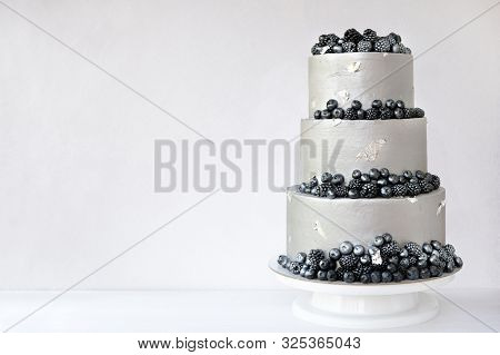 Wedding Cake With Silver Cream, Decorated With Blueberries And Blackberries On A White Wooden Backgr