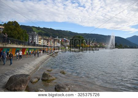 Zug, Switzerland 29.09.2019: People Walking, Relaxing At The Boardwalk On The Lake Zug Lakeshore Wit