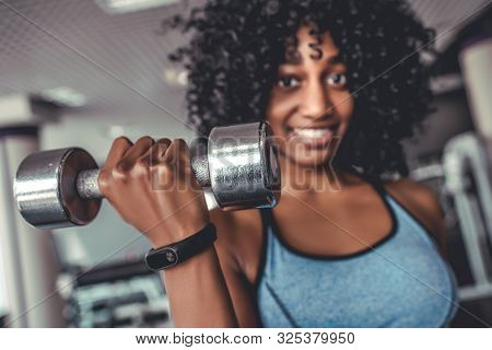 Portrait Of Smiling African Women Looking Camera In Gym Lifting Dumbbell. Yong Black Sportive Girl W