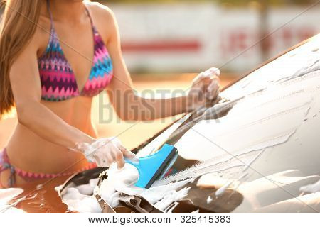 Young Woman In Swimsuit Washing Windshield Of Car With Squeegee Outdoors, Closeup