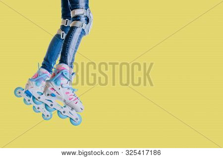 Childs Legs In Jeans And Roller Skates On A Yellow Background. Space For Text. Leisure And Sports.