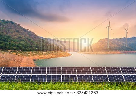 Solar Panels With Wind Turbines Against View Of The Reservoir And Mountanis Landscape Against During