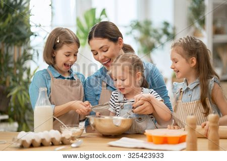 Happy loving family are preparing bakery together. Mother and children daughters girls are cooking cookies and having fun in the kitchen. Homemade food and little helpers.
