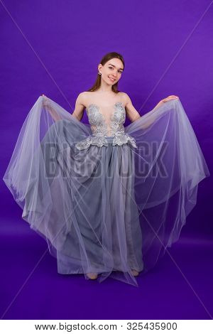 Young And Beautiful Woman Bride With Makeup In Long Chic Dress Posing In Studio On A Purple Backgrou