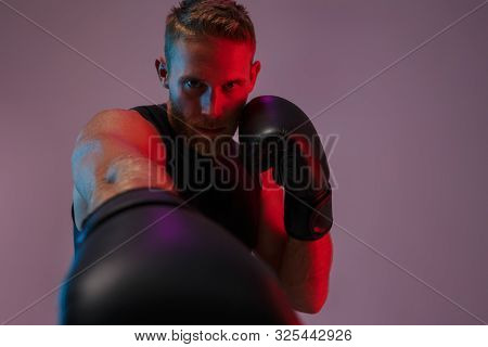 Image of a handsome strong young sports man boxer posing isolated over neon lights in gloves make boxing exercises.